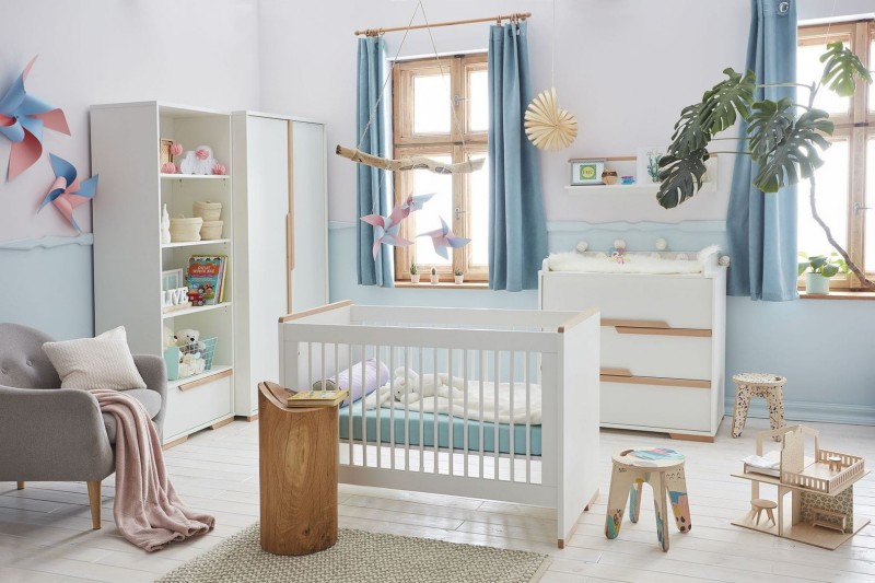 Biały zestaw mebli dziecięcych: łóżeczko, szafa, regał i komoda w jasnym, błękitnym pokoju.
