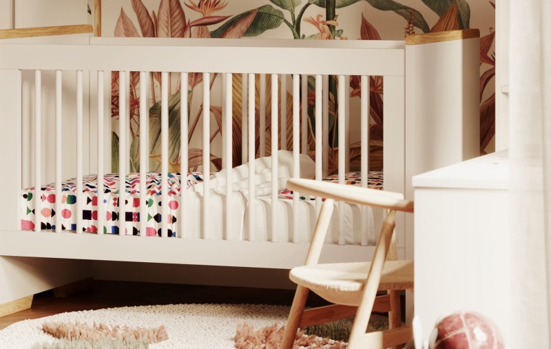 Białe łóżeczko dla niemowląt z drewnianym wykończeniem i wzorzystym materacem.