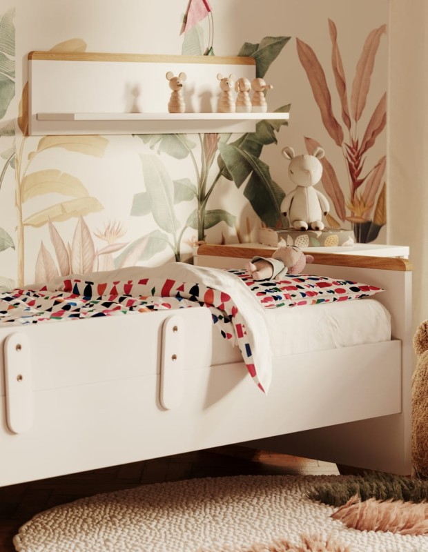 Białe łóżko dziecięce z kolorową pościelą na tle tapety w egzotyczne liście.