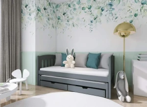Szare drewniane łóżko dziecięce z wysuwanym materacem i szufladami, w pokoju z tapetą w liście.