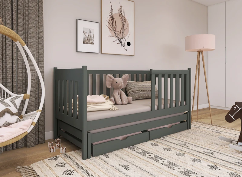 Ciemnoszare drewniane łóżko dziecięce z barierkami i szufladami, w pokoju dziecięcym z beżowymi ścianami.