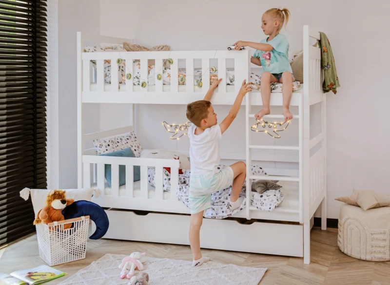 Dzieci bawiące się na białym drewnianym łóżku piętrowym w jasnym pokoju.