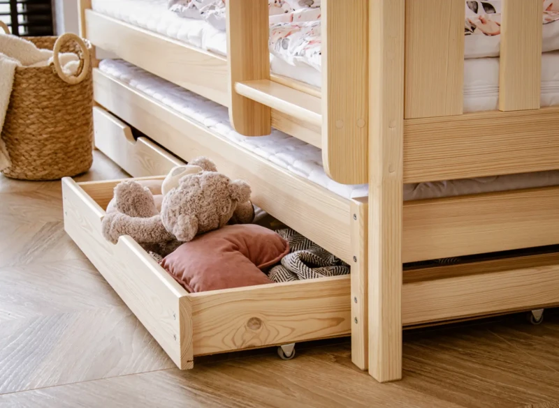 Zbliżenie na wysuwaną szufladę pod łóżkiem z pluszowym misiem.