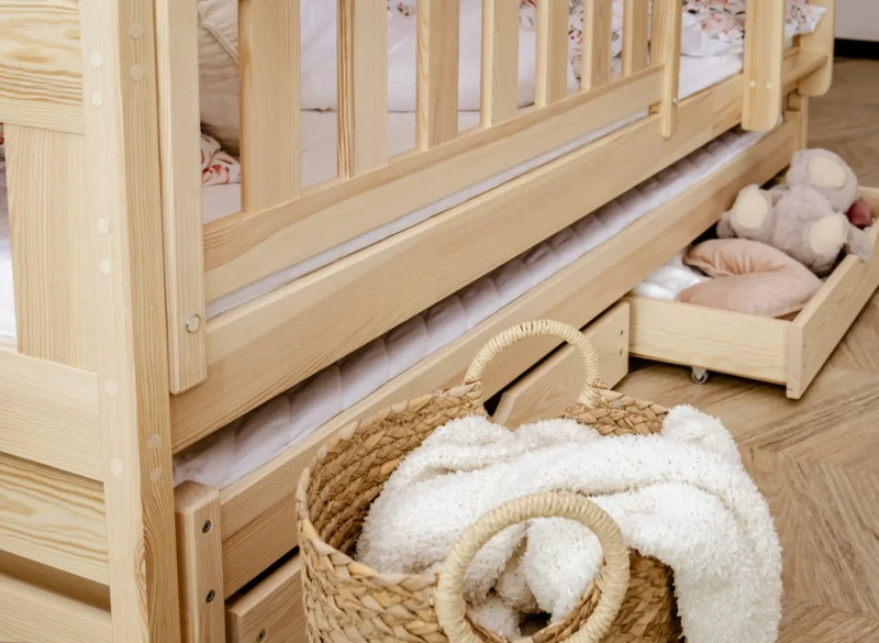 Dolna część łóżka piętrowego z koszem na koce i szufladą pełną zabawek.