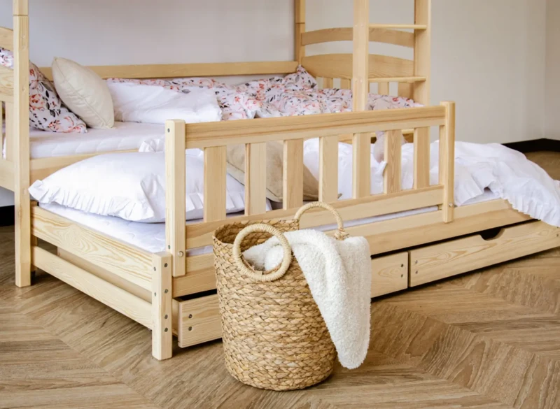 Łóżko piętrowe z wysuniętym dodatkowym spaniem i koszem wiklinowym w pokoju dziecięcym.