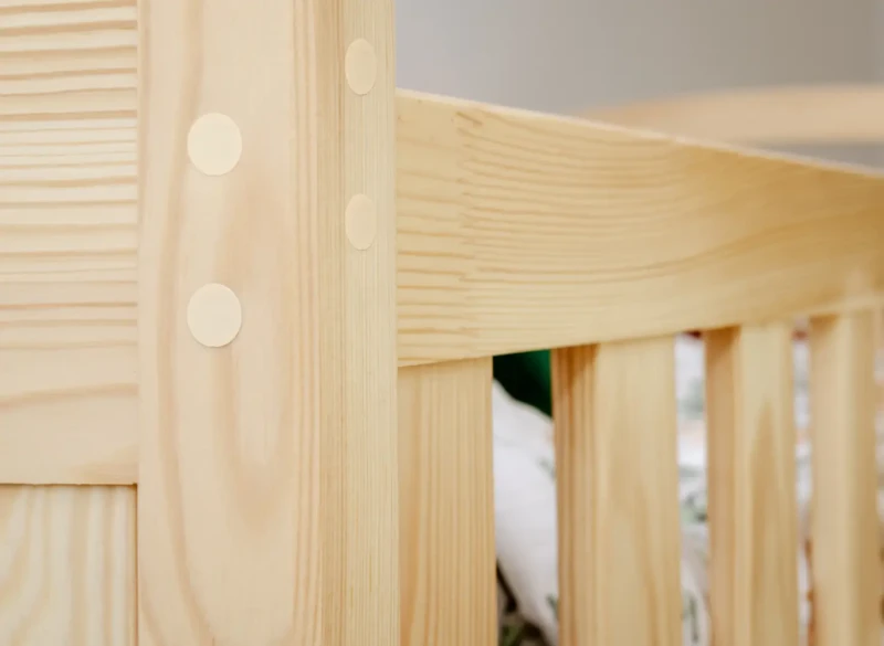 Zbliżenie na detale konstrukcyjne i naturalne drewno sosnowe łóżka dziecięcego.