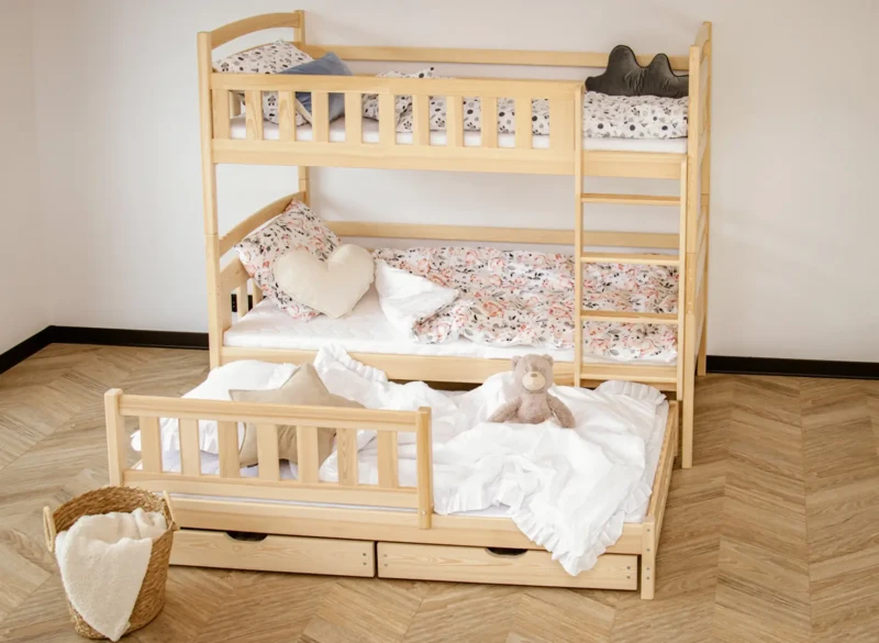 Trzyosobowe łóżko piętrowe z wysuwaną dostawką, białą pościelą i ozdobnymi poduszkami.