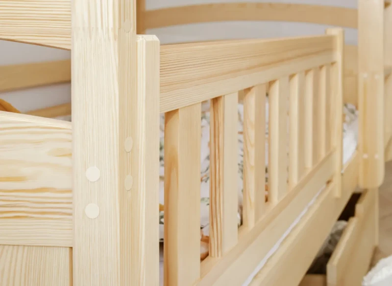 Zbliżenie na precyzyjne wykończenie i detale barierki ochronnej łóżka z litego drewna.