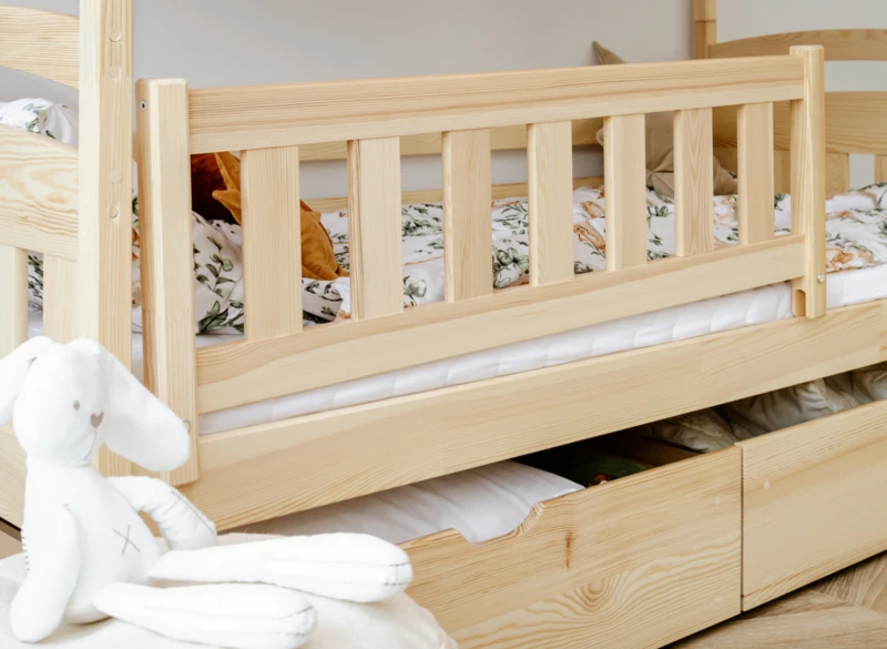 Zbliżenie na bezpieczną barierkę ochronną łóżka dziecięcego z naturalnego drewna sosnowego.
