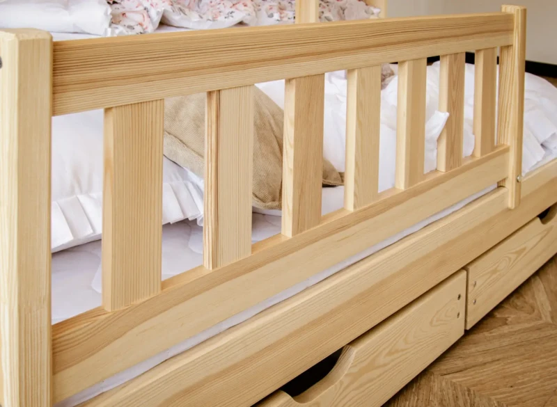 Drewniana barierka ochronna i funkcjonalne szuflady pod łóżkiem dla dzieci.