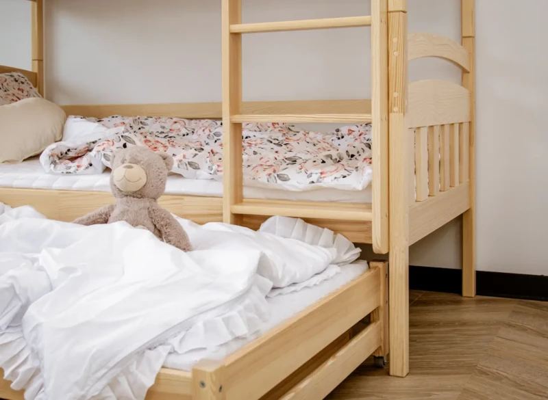 Drewniane łóżko piętrowe z dodatkowym wysuwanym miejscem do spania dla dzieci.