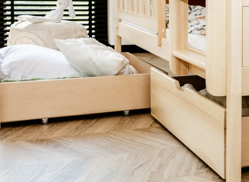 Szuflady na kółkach pod drewniane łóżko ułatwiające utrzymanie porządku w pokoju.