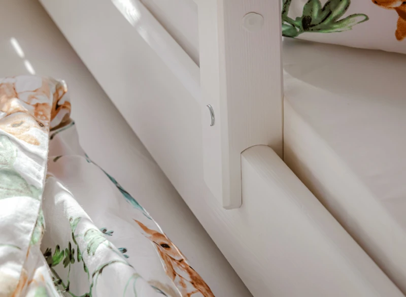 Zbliżenie na solidne łączenia i barierkę białego drewnianego łóżka dla dzieci.