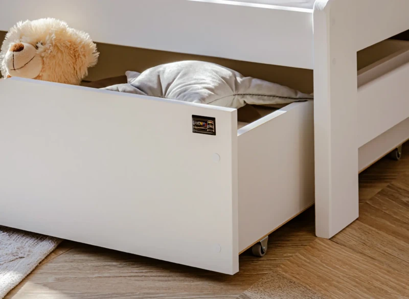 Otwarta szuflada pod łóżkiem dziecięcym z miejscem na pościel i pluszaki.