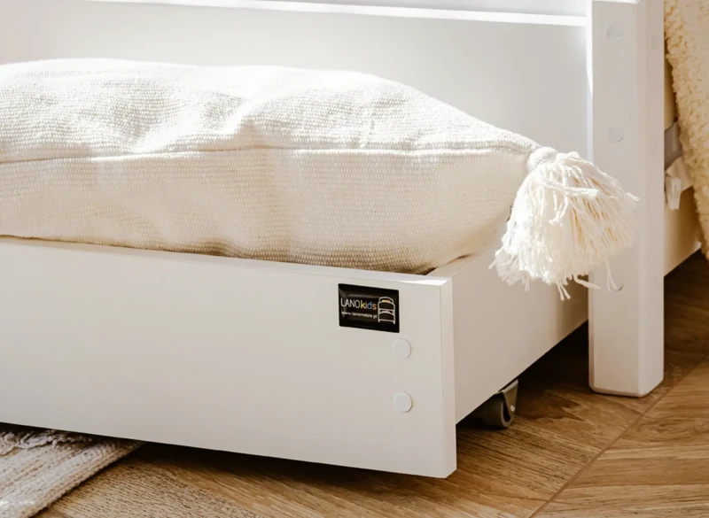 Szuflada pod białe łóżko dziecięce z logo LANO kids i dekoracyjną poduszką.