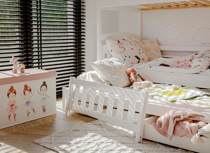 Białe łóżko piętrowe w pokoju dziewczynki obok skrzyni na zabawki.