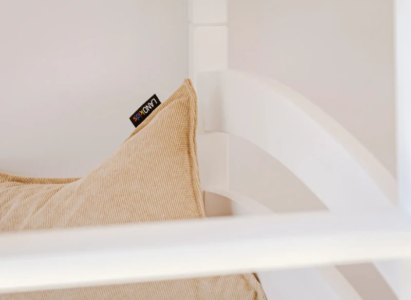 Beżowa poduszka z logo LANOkids na białej ramie łóżka dziecięcego.