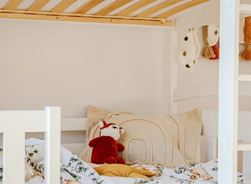 Przytulne dolne łóżko piętrowe z poduszką liskiem i wzorzystą pościelą.