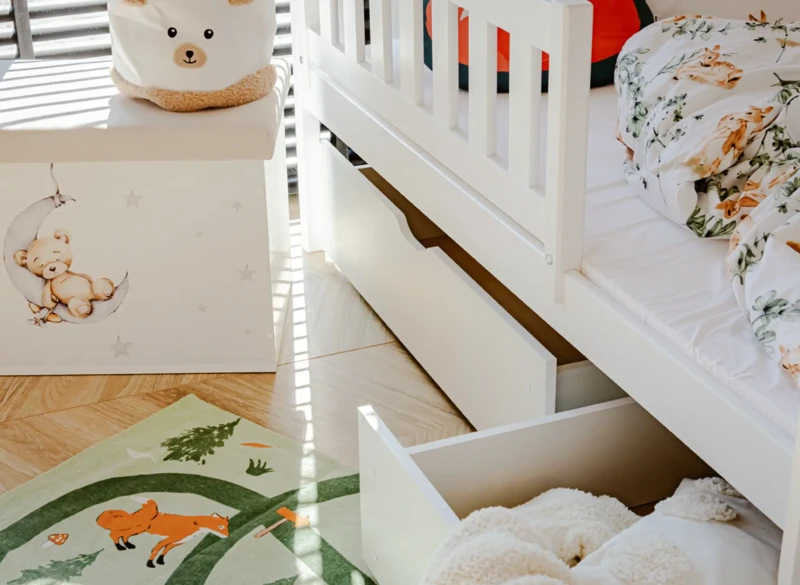 Praktyczne szuflady pod białym łóżkiem piętrowym na pościel i zabawki.