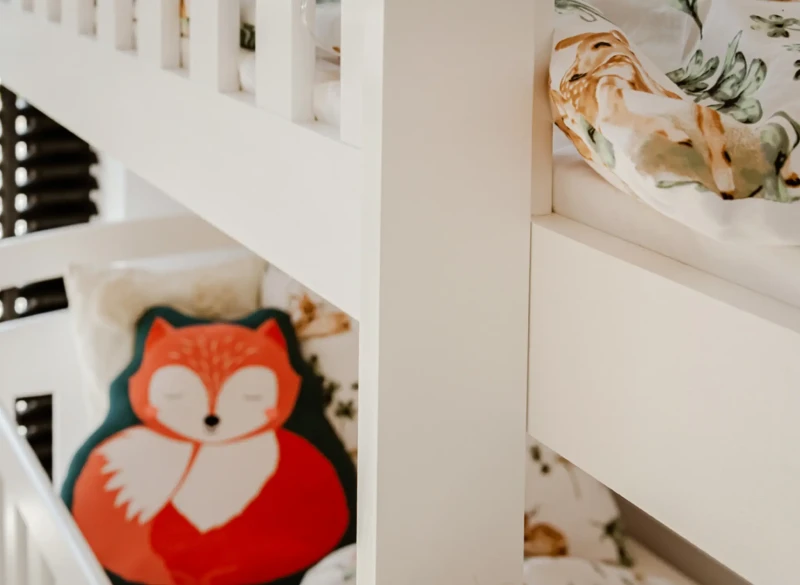 Solidna konstrukcja białego łóżka piętrowego z widoczną barierką i poduszką liska.