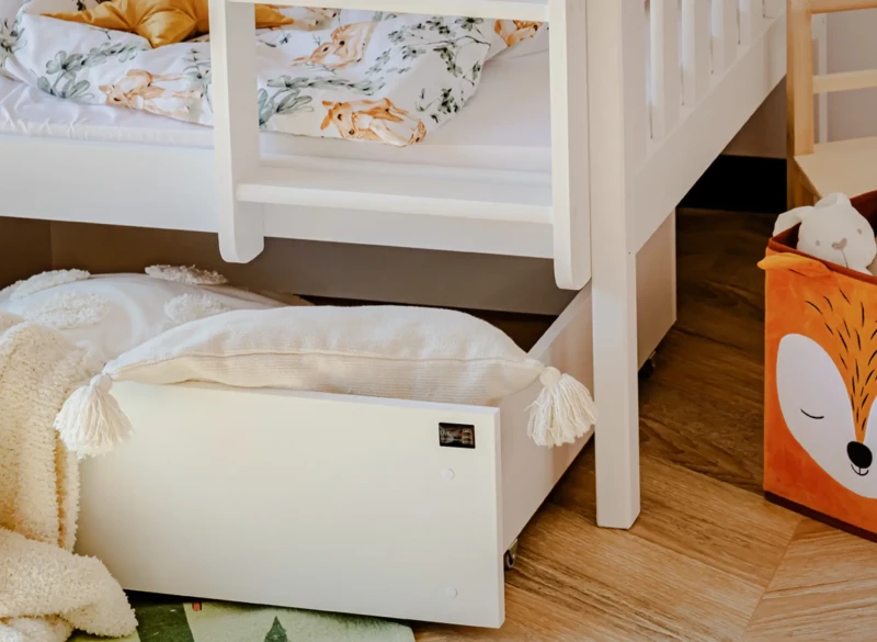 Praktyczna szuflada pod łóżkiem piętrowym wypełniona poduszkami i kocykiem.