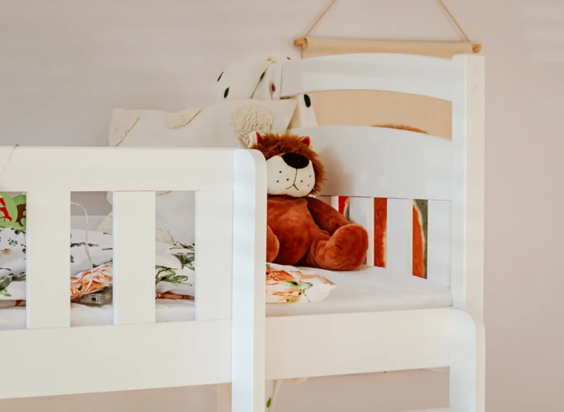 Górny poziom białego łóżka piętrowego z kolorową pościelą i misiem.