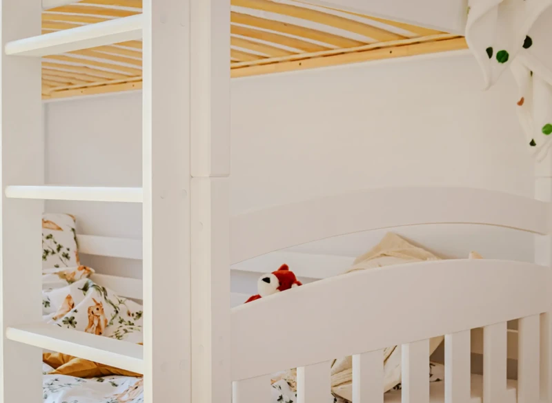 Białe łóżko piętrowe z drabinką i pościelą w leśne zwierzątka w pokoju dziecka.