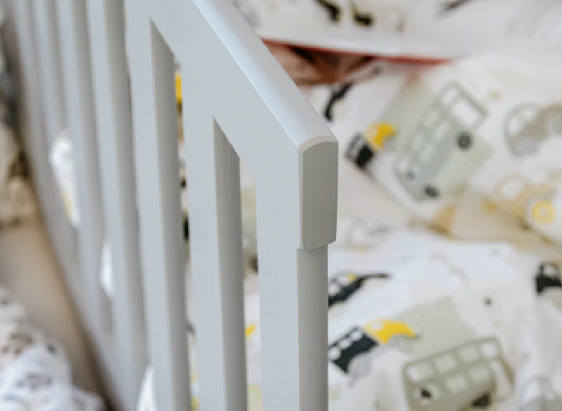 Bezpieczna barierka ochronna szarego łóżka dla dziecka.