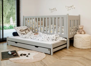 Szare drewniane łóżko dziecięce z barierkami, wysuwanym materacem i szufladami, w pokoju dziecięcym.