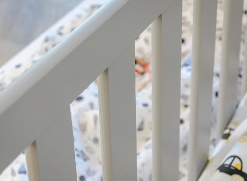 Zbliżenie na szare szczebelki drewnianego łóżka dziecięcego.