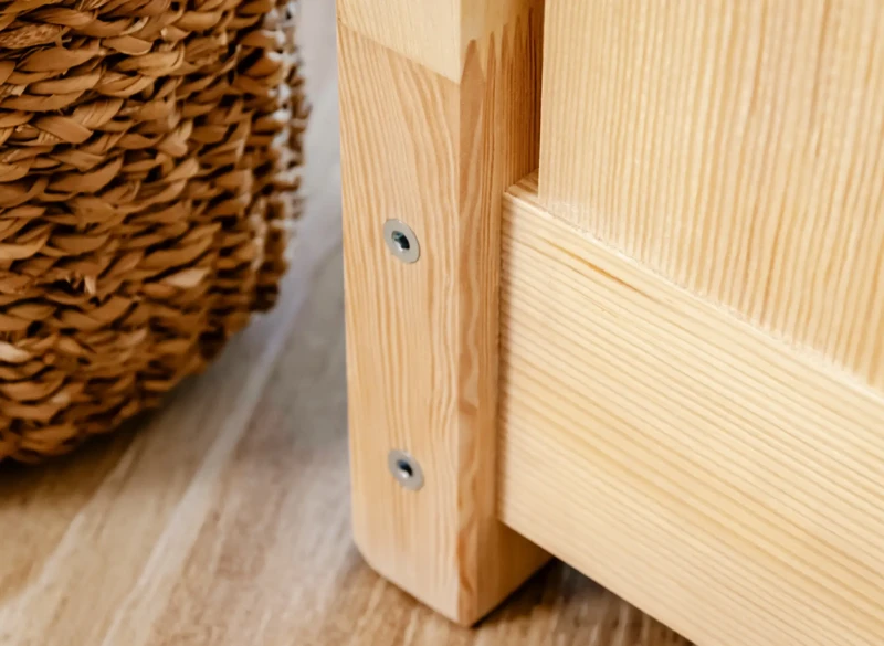 Solidne mocowanie ramy łóżka dziecięcego za pomocą śrub, widoczna tekstura drewna.