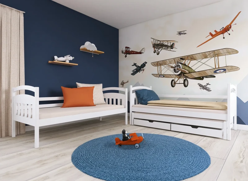 Białe drewniane łóżka dziecięce, jedno z wysuwanym materacem i szufladami, w pokoju z motywem lotniczym.