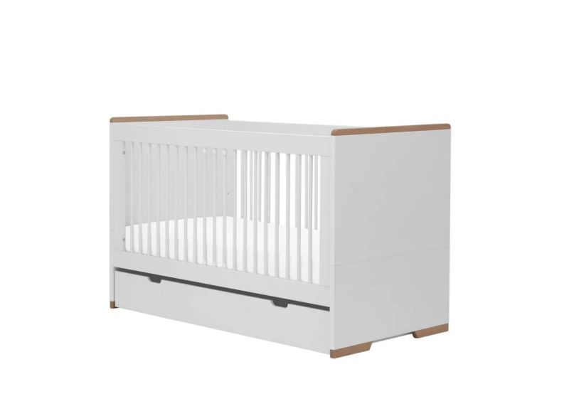 Białe łóżeczko niemowlęce ze szczebelkami i szufladą, z drewnianymi akcentami, na białym tle.