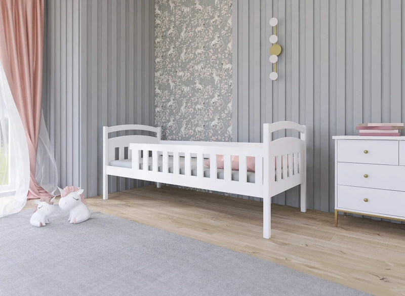 Białe drewniane łóżeczko dziecięce z barierką, w pokoju z szarą ścianą i tapetą w jednorożce.