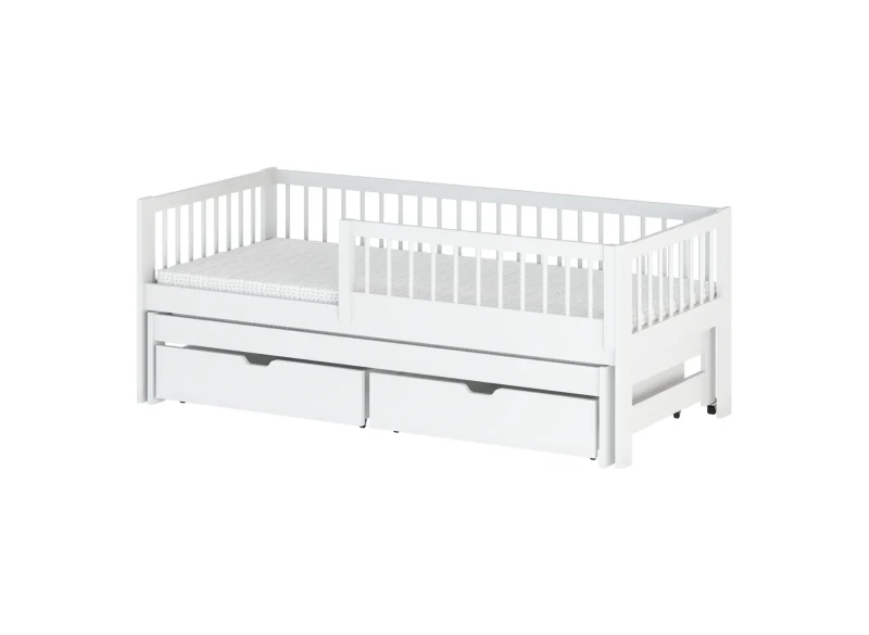 Białe drewniane łóżko ze szczebelkami, materac w biało-szare kropki, dwie białe szuflady pod spodem.