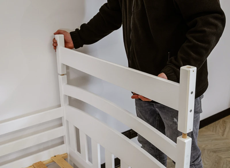 Montaż białego łóżka drewnianego - składanie ramy wezgłowia przez pracownika.