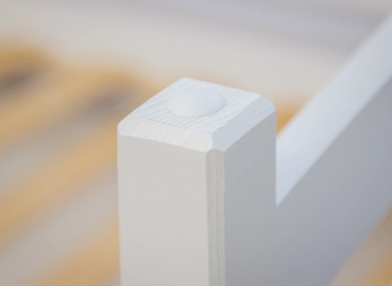 Biała zaślepka maskująca na górze słupka konstrukcyjnego łóżka drewnianego.