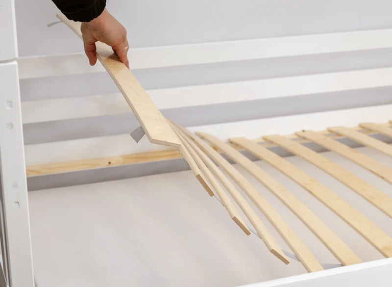 Rozkładanie elastycznego stelaża z listew brzozowych na białej ramie łóżka.