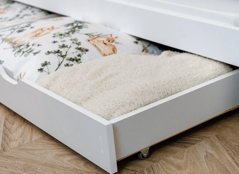 Detal wysuwanej szuflady na kółkach pod łóżko z miejscem na pościel.