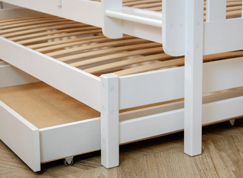 Białe drewniane łóżko piętrowe ze stelażem i wysuwaną szufladą na kółkach.