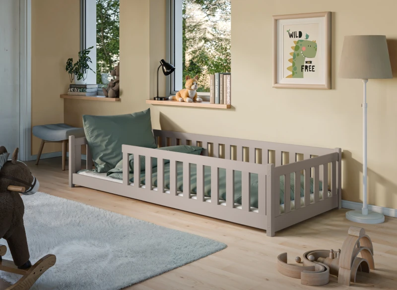 Szare łóżko dziecięce z drewna z barierkami, z zieloną pościelą, w aranżacji pokoju z żółtymi ścianami.