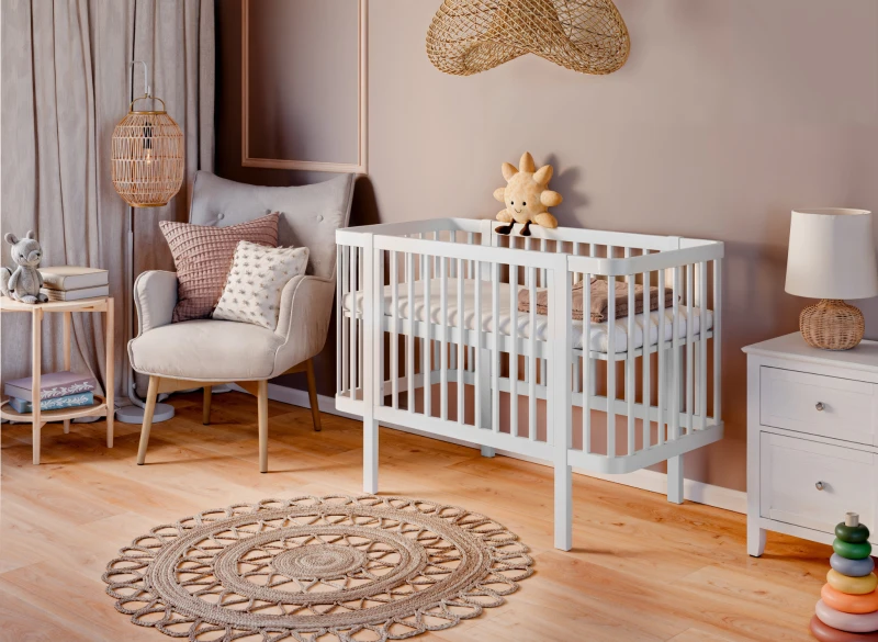 Nowoczesne białe łóżeczko dla niemowląt z drewna, z pluszową zabawką, w jasnym pokoju dziecięcym.