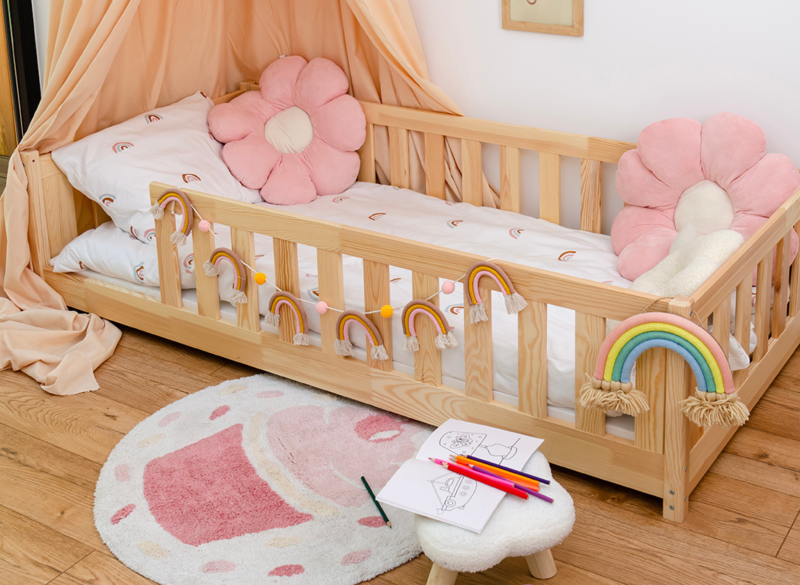 Drewniane łóżko dla dziewczynki z baldachimem i poduszkami w kształcie kwiatów.