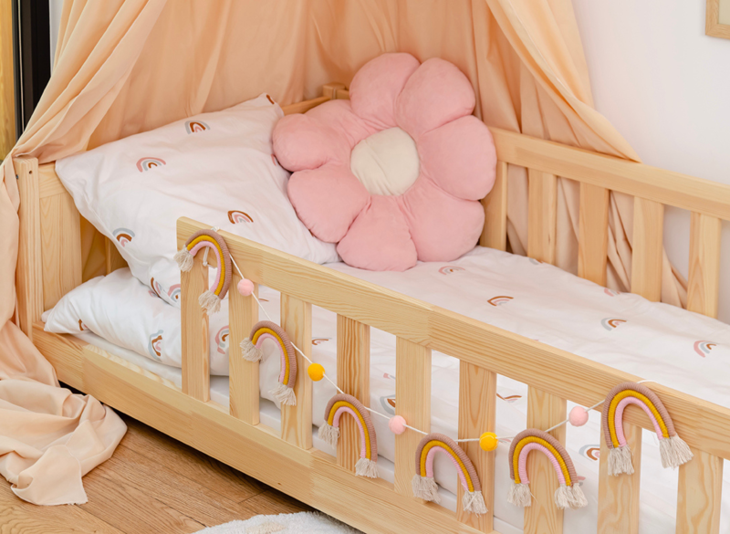 Detal drewnianego łóżka dziecięcego z ozdobną girlandą i różową poduszką.