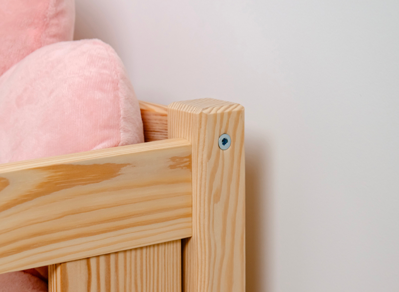 Wykończenie narożnika drewnianego łóżka z różową poduszką w tle.