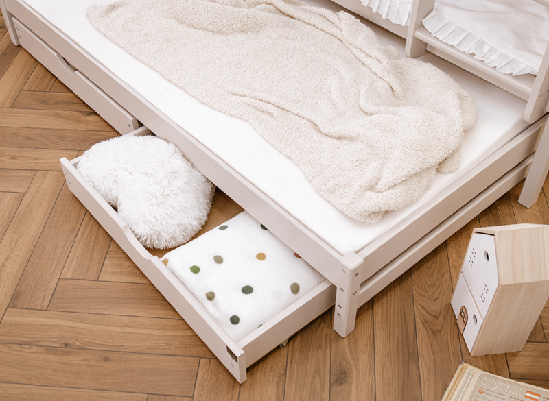 Otwarta szuflada pod łóżkiem dziecięcym idealna do przechowywania pościeli.