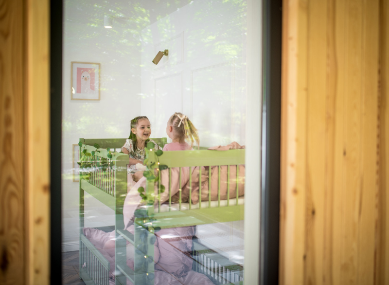 Dwie dziewczynki bawiące się na zielonym łóżku piętrowym w przytulnym pokoju dziecięcym.