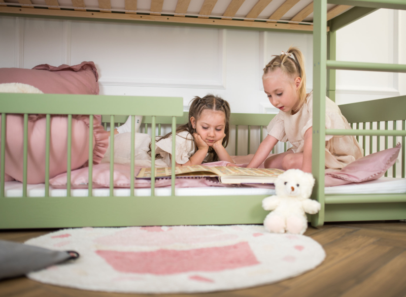Siostry wspólnie czytające książkę na dolnym poziomie bezpiecznego łóżka piętrowego.