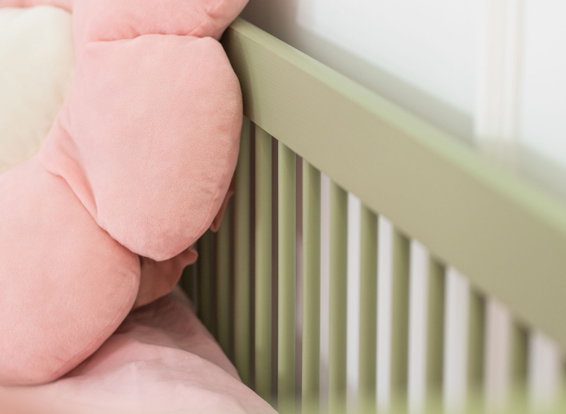 Bezpieczna barierka z pionowymi szczebelkami w zielonym łóżku dziecięcym.