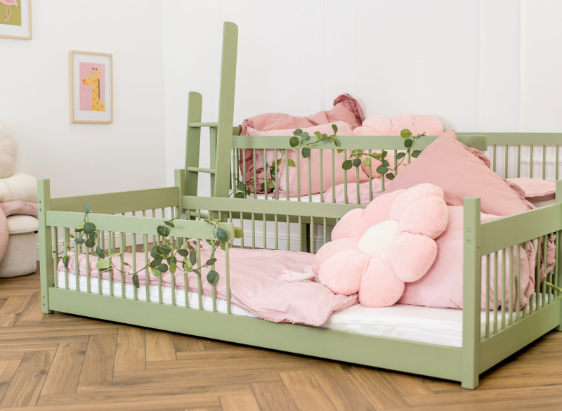 Oliwkowe łóżko dziecięce z barierkami i różową pościelą